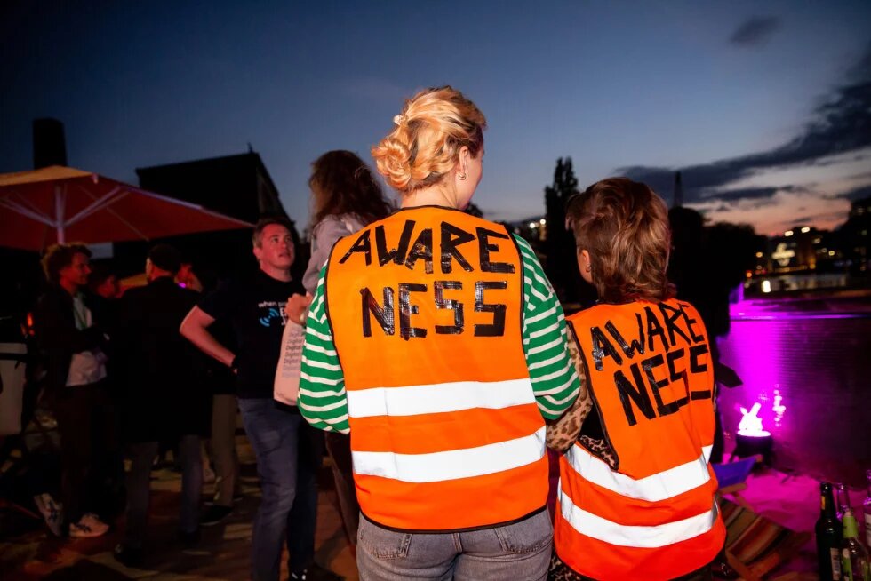 Zwei Personen mit Awareness-Warnwesten stehen mit dem Rücken zum Betrachter, vor einer Festivalkulisse